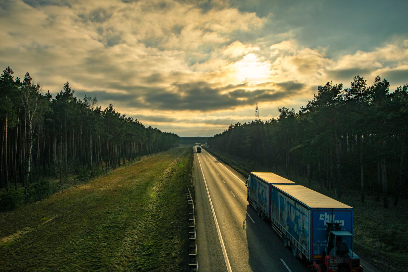 Trucks on a highway flanked by forest at sunset